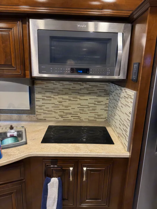 RV rental kitchen: Whirlpool microwave, induction cooktop, and tiled backsplash within rich wood cabinetry.. Thor Venetian 2017