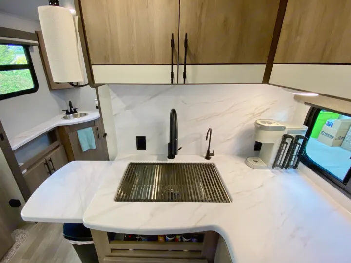 RV rental kitchen with white marble countertops, large sink, sleek black faucets, and modern overhead cabinets.. Grand Design Imagine 2023