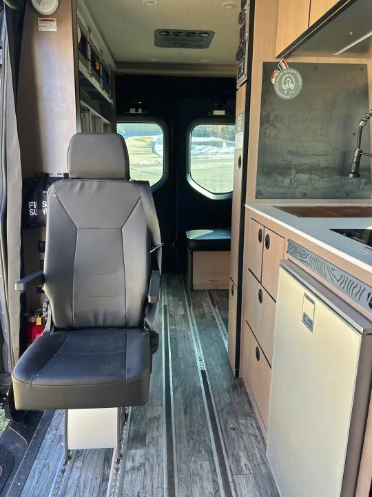View inside an RV rental showing a front swivel seat, compact kitchen, and floor tracks for adaptable living.. Antero Adventure Motors Antero Adventure Motors Class B 2022