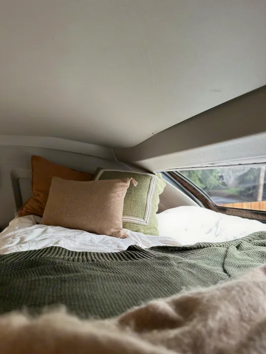 This RV rental offers a cozy bed: white sheets, green knit blanket, and comfy pillows visible inside a vehicle.. Coachmen Prism Select 2023