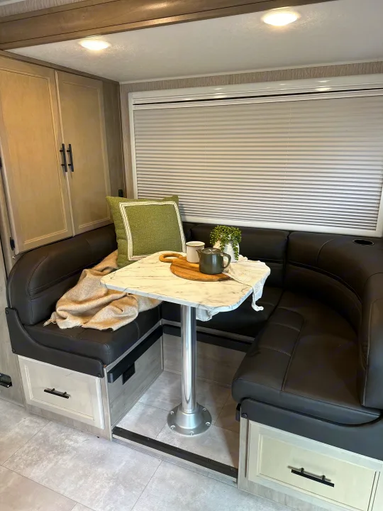 Cozy RV rental dinette with U-shaped seating, storage, and a light-filled window, perfect for compact living.. Coachmen Prism Select 2023