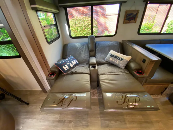 An RV rental's living area features two comfy recliners with footrests & red-lit cup holders, cozy throws, and decorative pillows.. Grand Design Imagine 2023