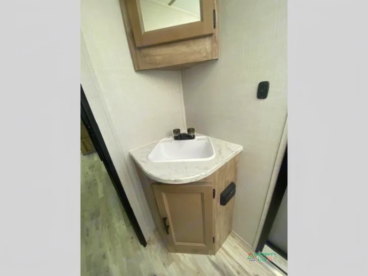 This RV rental features a compact bathroom with a corner sink, base cabinet, and mirrored medicine cabinet.. Gulf Stream Friendship 268BH 2024