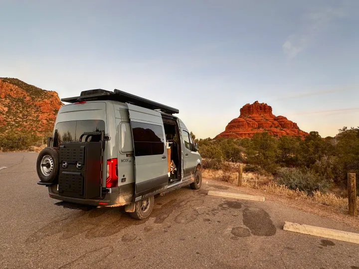 Adventure awaits! This grey RV rental camper van is parked amidst Sedona's stunning red rocks with a dog on board.. Storyteller Overland Storyteller Overland Class B 2023