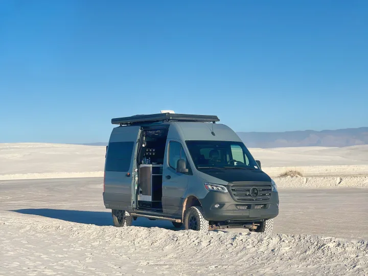 This gray Mercedes-Benz RV rental, a camper van with off-road tires, is parked on white gypsum dunes under a clear blue sky.. Storyteller Overland Storyteller Overland Class B 2023