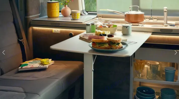 Inside an rv rental: a cozy camper kitchen and dining area with a meal laid out, perfect for road trip comfort.. Volkswagen California T6.1 DSG 2024