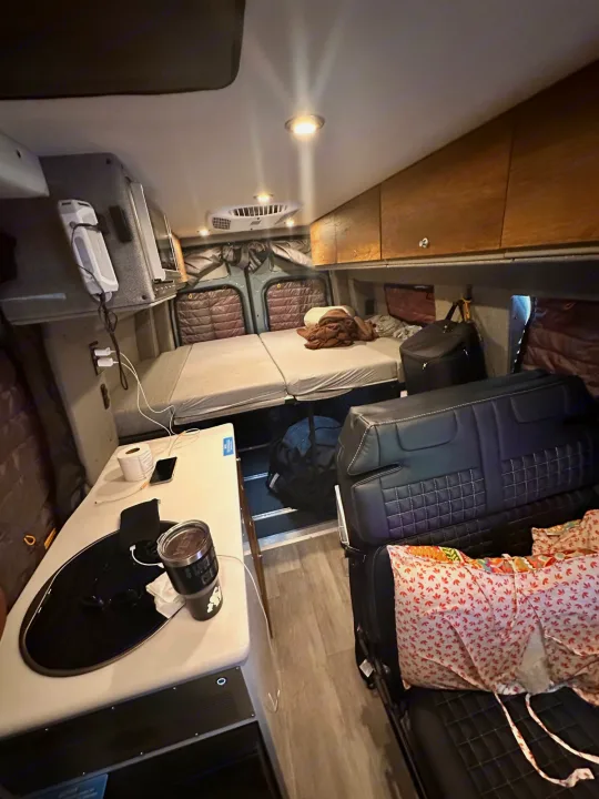 Cozy RV rental interior shows a compact bed, kitchen counter with sink, and a seating area for comfortable travel.. Storyteller Overland Storyteller Overland Class B 2023