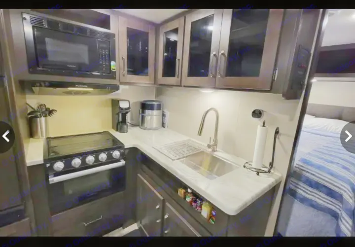 Inside an RV rental: a modern kitchen with a microwave, stove, sink, and cabinets, ready for your next adventure.. Grand Design Other 2022