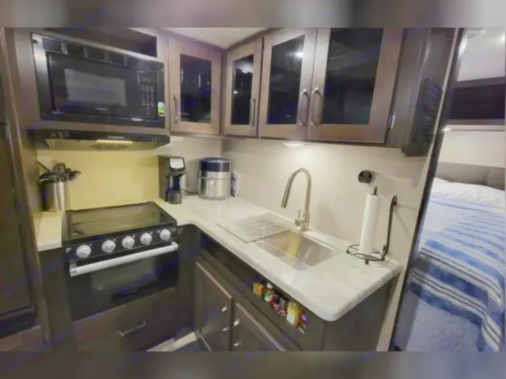 RV rental interior: a compact kitchen with microwave, stove, sink, and an adjacent bedroom with a striped bed.. Grand Design Other 2022