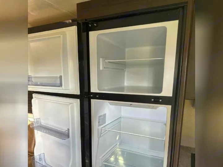 Clean, empty RV rental refrigerator with top freezer and lower fridge compartments open, ready for use.. Grand Design Other 2022