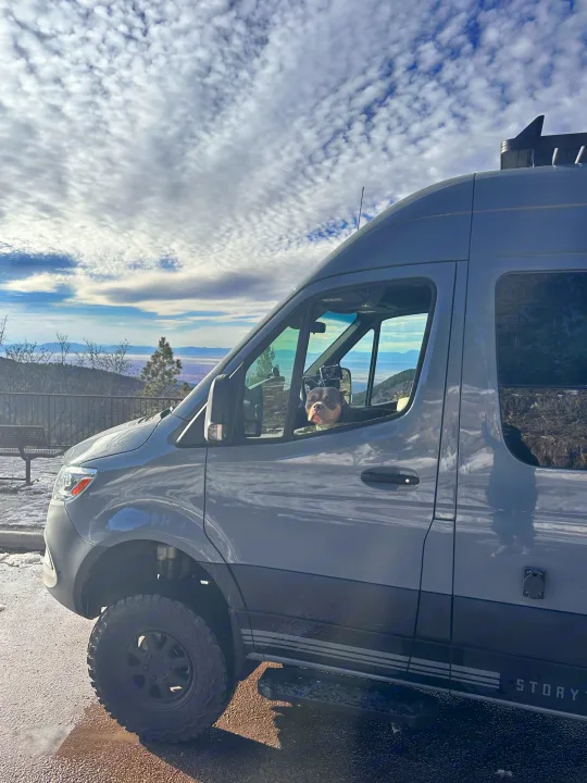 Off-road gray **RV rental** van with a dog peeking out, parked at a snowy mountain overlook.. Storyteller Overland Storyteller Overland Class B 2023