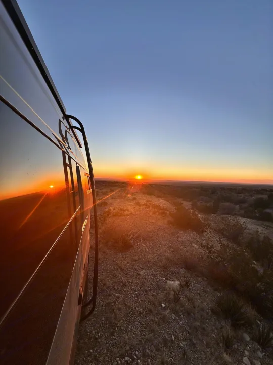 An RV rental reflects a vibrant desert sunset, parked on a rocky hill overlooking a vast landscape.. Storyteller Overland Storyteller Overland Class B 2023
