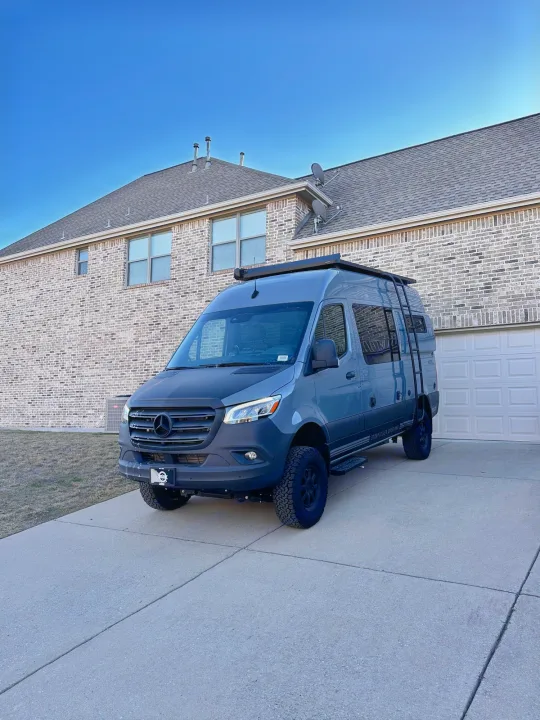Gray Mercedes-Benz Sprinter camper van, ideal for an RV rental, parked on a driveway in front of a brick house.. Storyteller Overland Storyteller Overland Class B 2023