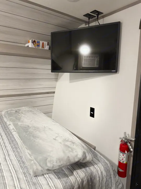 Cozy RV rental interior featuring a neatly made bed, wall-mounted Vizio TV, and a red fire extinguisher for safety.. Coleman Lantern LT 17B 2024