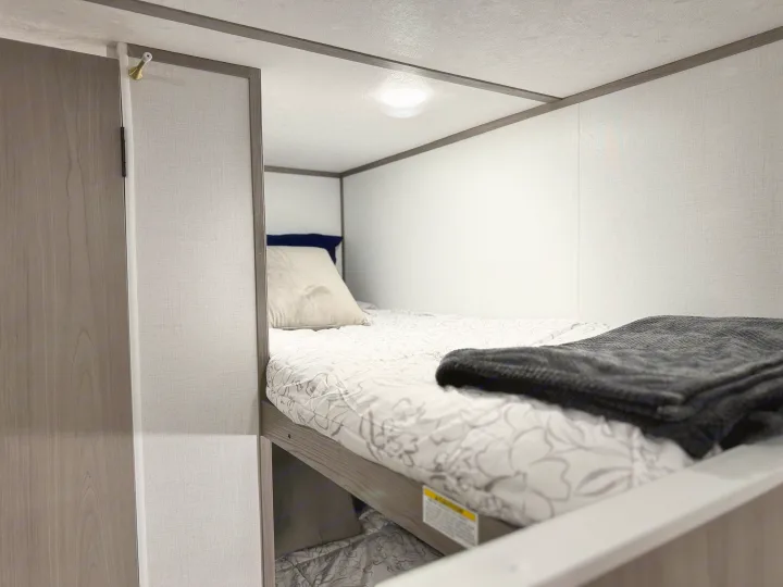 Cozy lower bunk bed in an rv rental, featuring a mattress, pillow, and dark blanket for a restful sleep.. Coleman Lantern LT 17B 2024