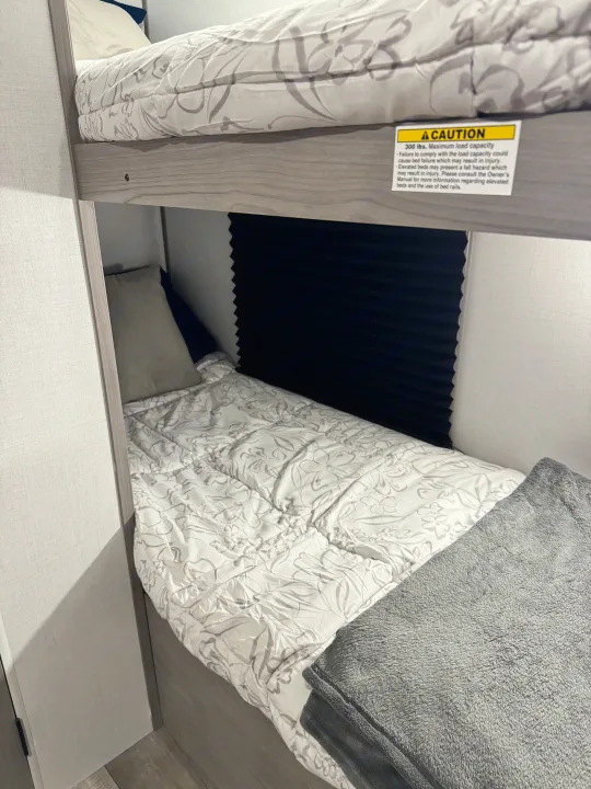 An RV rental's cozy bunk beds, featuring a top bunk with a 300 lbs. capacity safety label for elevated bed safety.. Coleman Lantern LT 17B 2024