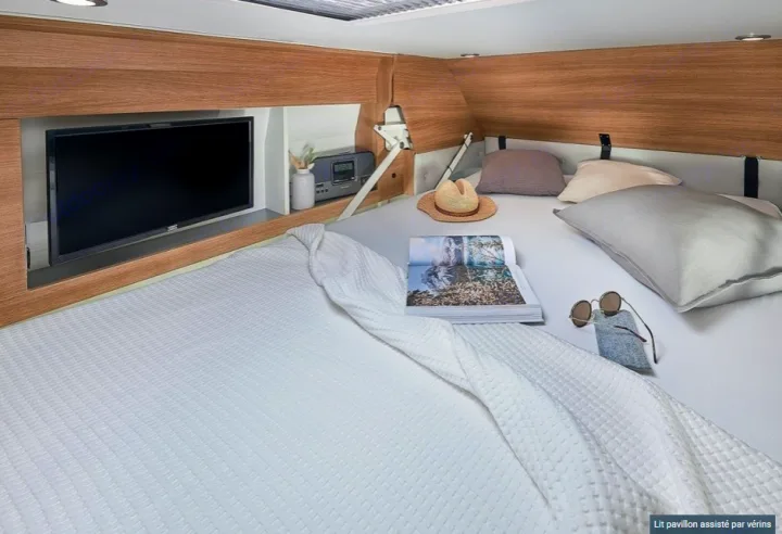 Relax in this modern RV rental bedroom featuring a comfy bed, integrated TV, and warm wood finishes.. CAMPEREVE FAMILY VAN 2022