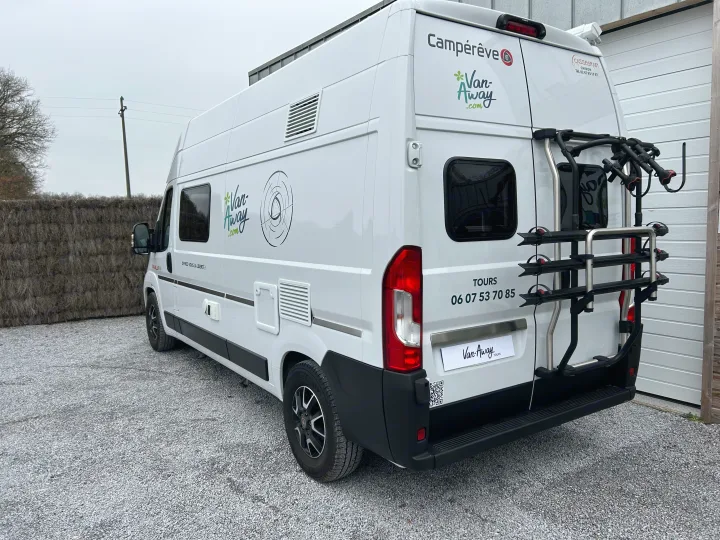 A white Van-Away camper van with bike rack parked on gravel. Ideal for RV rental adventures and leisure travel.. CAMPEREVE FAMILY VAN 2022