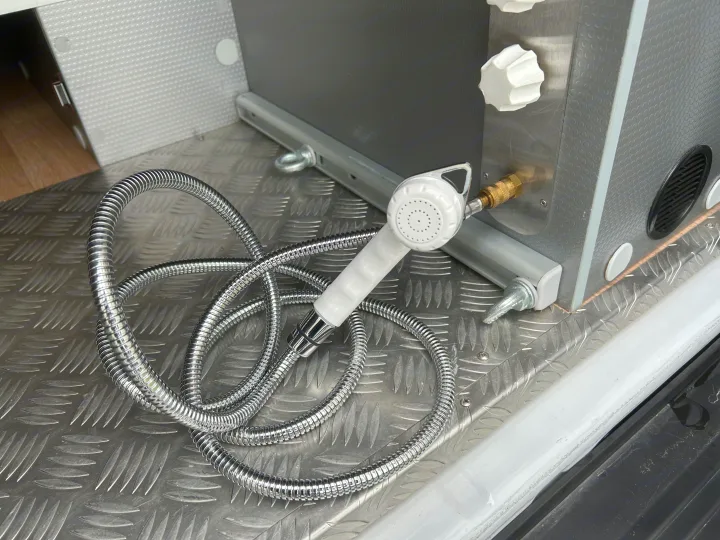RV rental outdoor shower unit with white spray head, metallic hose & water controls on a diamond plate floor.. CAMPEREVE FAMILY VAN 2022