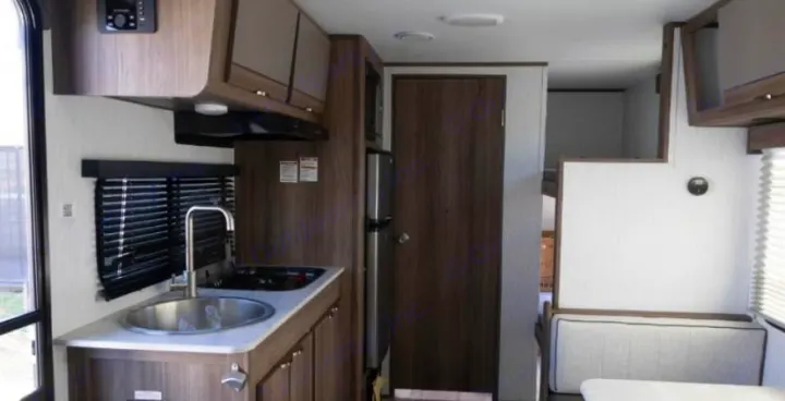 Compact RV rental interior featuring a kitchen with sink/stove, refrigerator, and a cozy dinette/bunk area.. Cruiser RV Hitch 2024