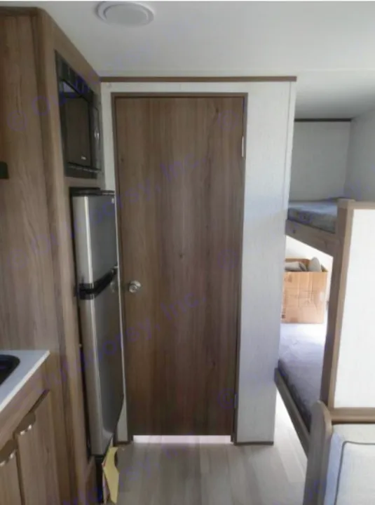 RV rental interior: compact kitchen (fridge, microwave) on left, door in middle, and bunk beds on right.. Cruiser RV Hitch 2024