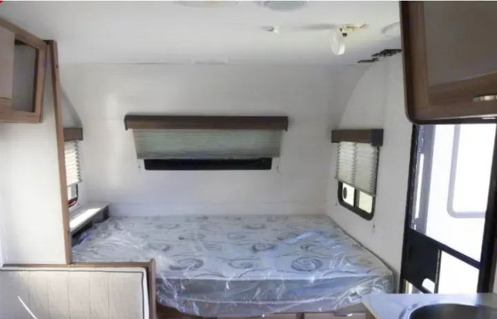 View of an RV rental bedroom with a plastic-covered mattress, windows with blinds, and built-in cabinets.. Cruiser RV Hitch 2024