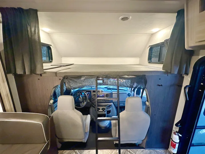 Interior of an rv rental: large overhead bunk bed with ladder, overlooking the driver's cabin and front seats.. Forest River Sunseeker LE 2023
