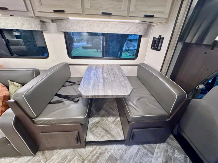 Spacious RV rental dinette with comfortable gray seating, large table, and bright windows. Perfect for dining & relaxation.. Forest River Sunseeker LE 2023