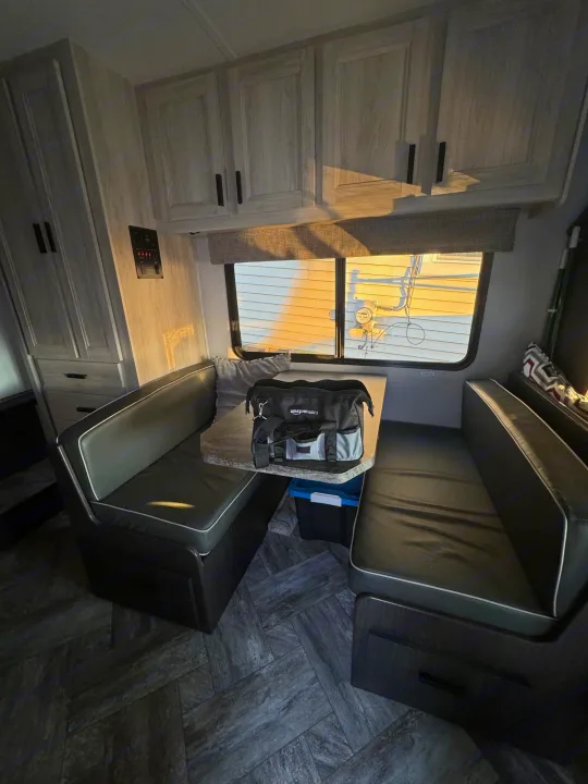 Inside an RV rental: a bright dinette area with built-in benches, a table, and light-colored cabinetry by a sunny window.. Forest River Sunseeker LE 2022