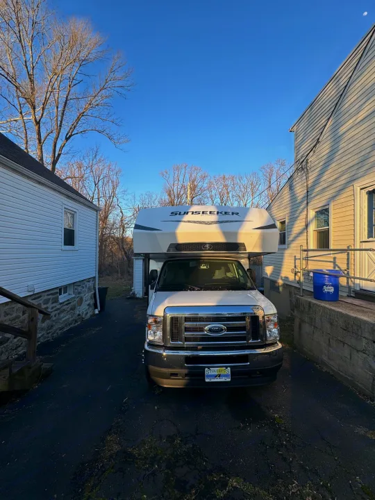 A white Ford Sunseeker RV rental parked on an asphalt driveway between two homes under a clear blue sky.. Forest River Sunseeker LE 2022