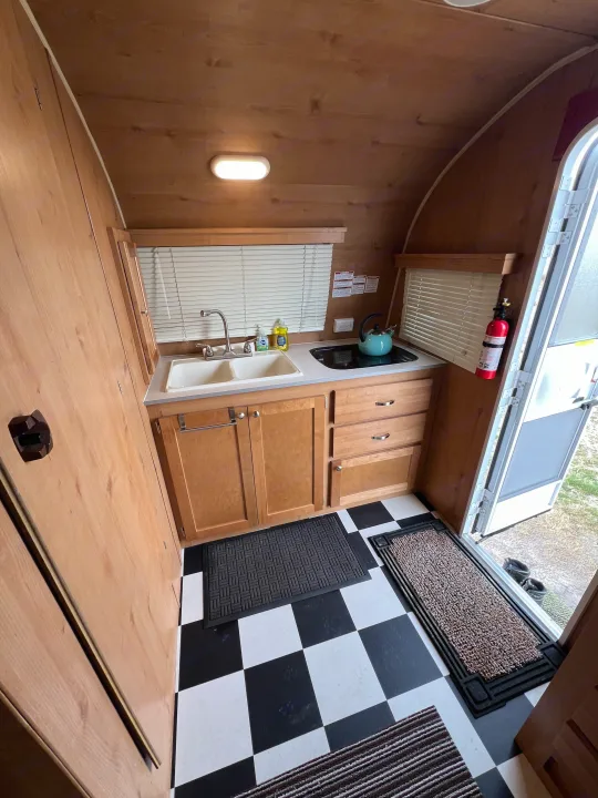Compact RV rental kitchen interior featuring a sink, cooktop, wood cabinetry, and checkerboard floor. Essentials for your trip!. Riverside Travel Trailer 157 Retro 2018