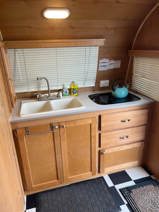 Functional RV rental kitchen with a double sink, modern stovetop, wood cabinetry, bright light, and checkered floor.. Riverside Travel Trailer 157 Retro 2018