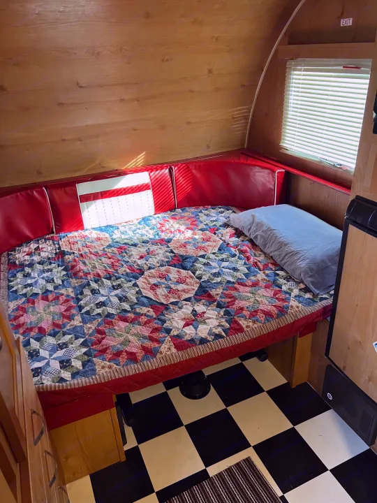 Cozy RV rental interior with a patchwork quilt bed, red cushions, wood paneling, and checkered floor. Perfect for a road trip!. Riverside Travel Trailer 157 Retro 2018