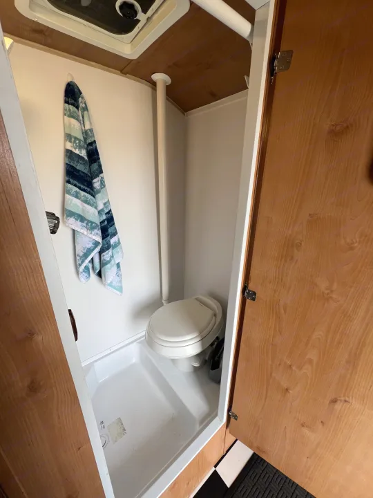Compact RV rental bathroom featuring a toilet, shower pan, and overhead vent, with a towel hanging.. Riverside Travel Trailer 157 Retro 2018