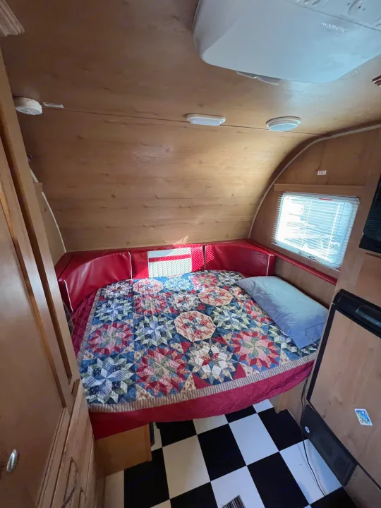 Inviting RV rental interior: a comfy bed with a vibrant quilt, red cushions, and classic checkered flooring.. Riverside Travel Trailer 157 Retro 2018