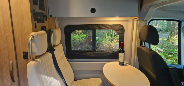 Relaxing rv rental space: comfortable seating, a table with wine, and a serene forest view through the window.. Winnebago Solis 2022