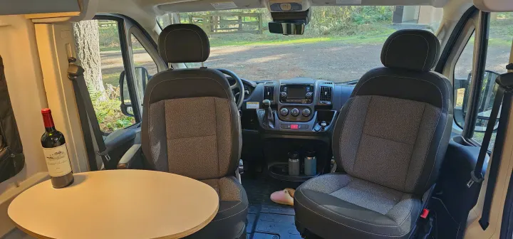 Inside an RV rental: front cabin with seats, dash, and a cozy table. Ready for a scenic road trip adventure.. Winnebago Solis 2022