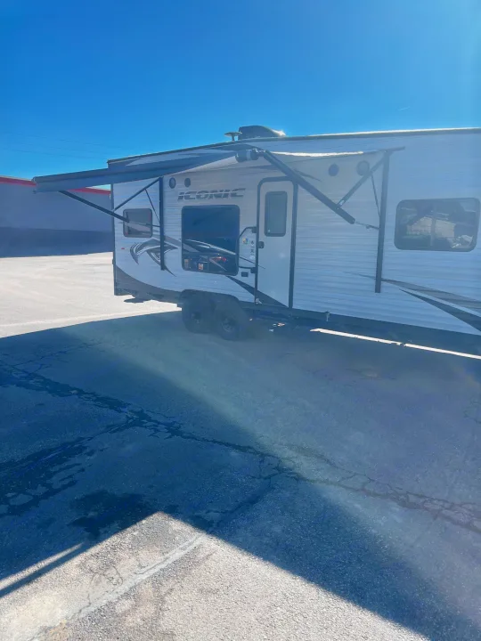 Side view of a white ICONIC travel trailer RV with awning extended, parked on asphalt. Ideal for rv rental.. Eclipse Recreational Vehicles Iconic 2018