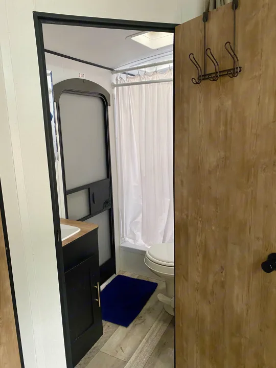 Compact RV rental bathroom: features shower, toilet, and sink area. Note the exit door and convenient coat hooks.. Keystone RV Springdale 2022