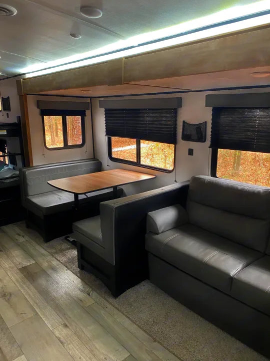 Inside a modern RV rental: a comfortable dinette, gray sofa, and light wood-look flooring under bright ceiling lights.. Keystone RV Springdale 2022