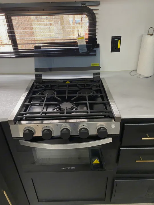 RV rental kitchen: modern Greystone gas stove, oven, and cooktop with glass cover raised, ready for cooking.. Keystone RV Springdale 2022