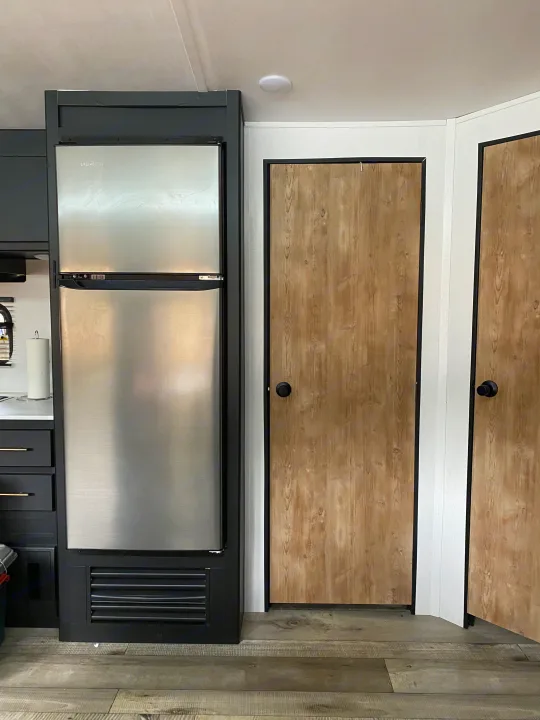 Interior of an RV rental featuring a stainless steel refrigerator, black cabinetry, and two wood-look doors.. Keystone RV Springdale 2022