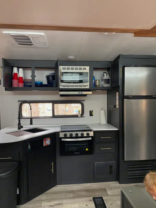 Inside an RV rental: a modern kitchen with black cabinets, light countertops, stainless appliances, and a pull-down faucet by a window.. Keystone RV Springdale 2022