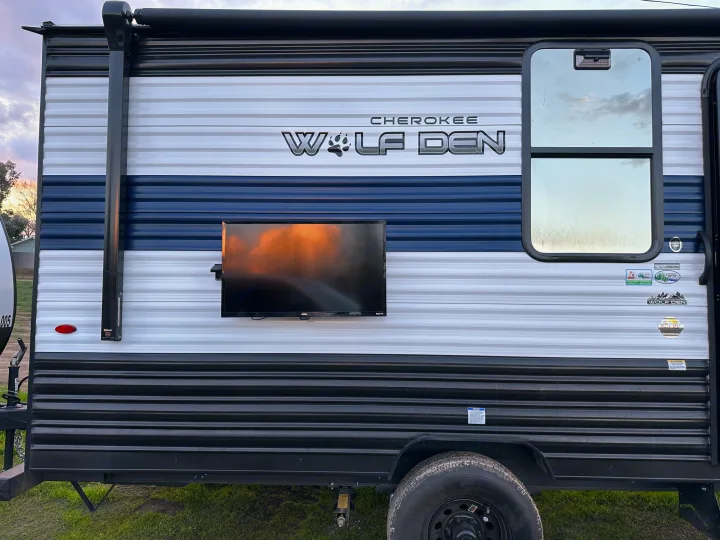 Cherokee Wolf Den RV rental side view with outdoor TV, awning, and distinctive white, blue, and black stripe pattern.. Forest River Cherokee Wolf Den 16 EV 2024