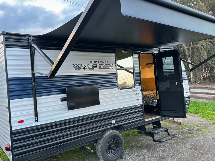 Cherokee Wolf Den RV rental, featuring an extended awning, outdoor TV, and open door showing the cozy interior.. Forest River Cherokee Wolf Den 16 EV 2024