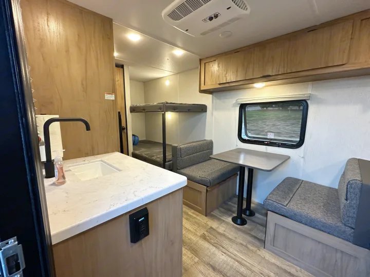 This modern RV rental interior features a kitchen with a sink, bunk beds, and a dinette seating area, ideal for your camper road trip.. Forest River Cherokee Wolf Den 16 EV 2024