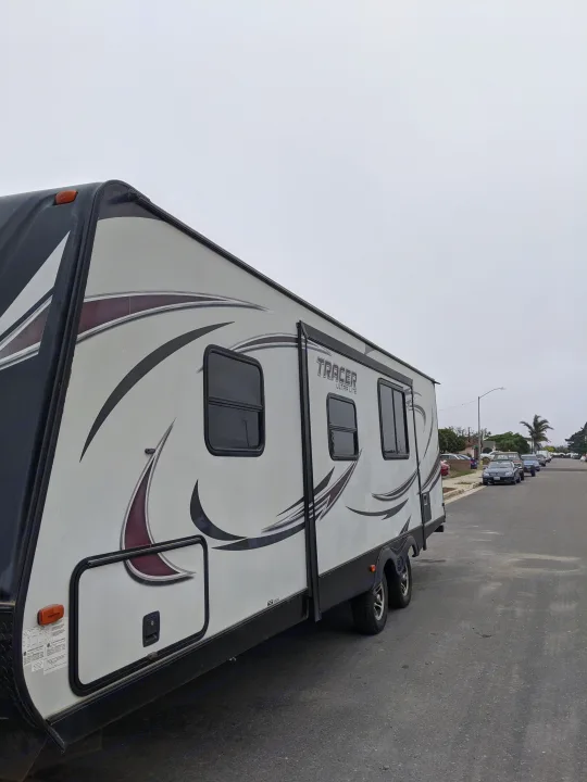 A 'TRACER ULTRA LITE' travel trailer, possibly an RV rental, parked on a residential street under an overcast sky.. Other Other 2015