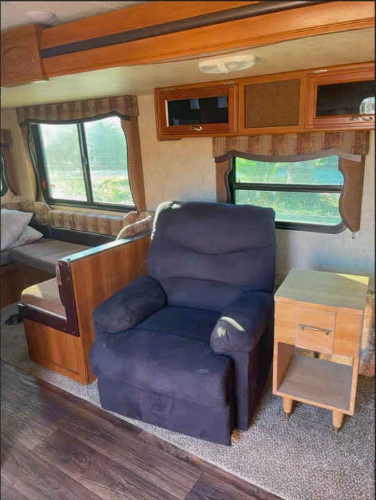 Inside a cozy RV rental: a plush dark recliner, wooden dinette, and large windows illuminate the comfortable living area.. Other Other 2015