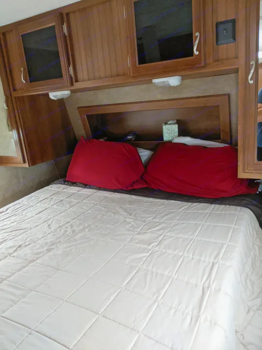 Cozy RV rental bedroom with a comfy bed, red pillows, and convenient built-in storage for a relaxing travel experience.. Other Other 2015