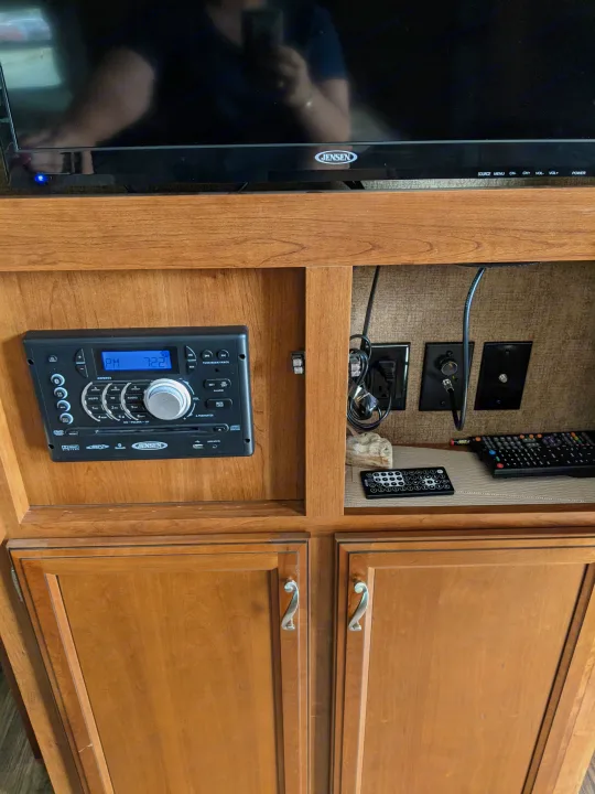 An RV rental's entertainment setup featuring a Jensen TV, AWM968 stereo, and remotes within wooden cabinetry.. Other Other 2015
